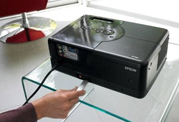 Epson EH-DM2 LCD projector on glass table with hand pressing button.