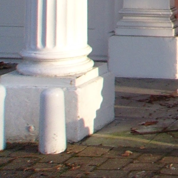 Close-up of a column base with shadows and leaf debris.
