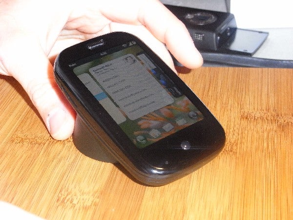 Palm Pre smartphone on wooden surface with hand above it.