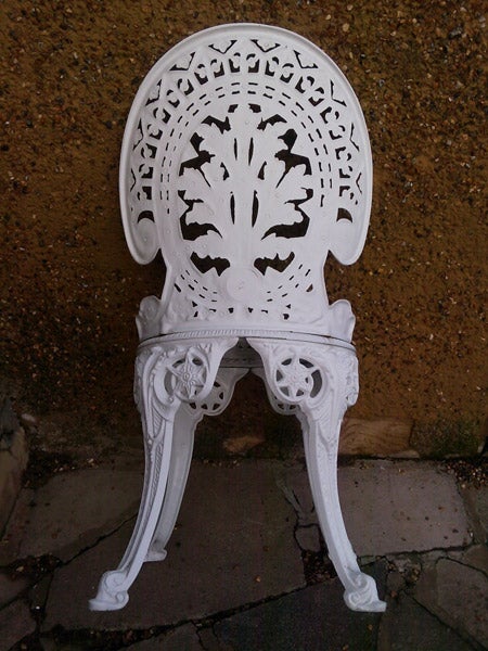 White ornate cast iron chair against a wall.
