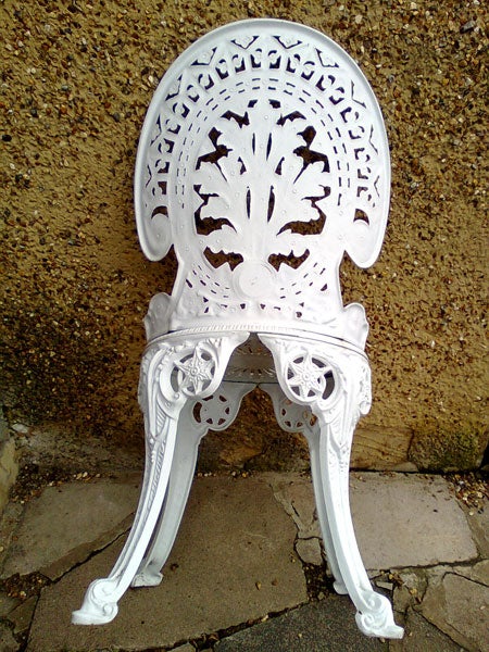Intricately designed white cast iron chair against a textured wall.