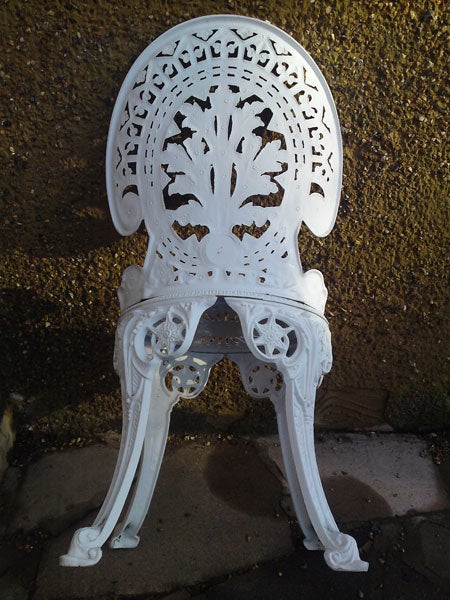 White cast iron chair with decorative backrest against a wall.