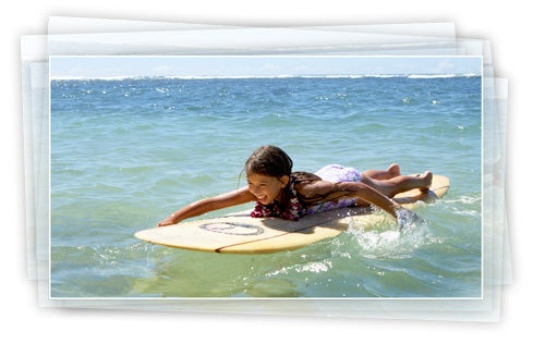 Child playing on a surfboard in the ocean.
