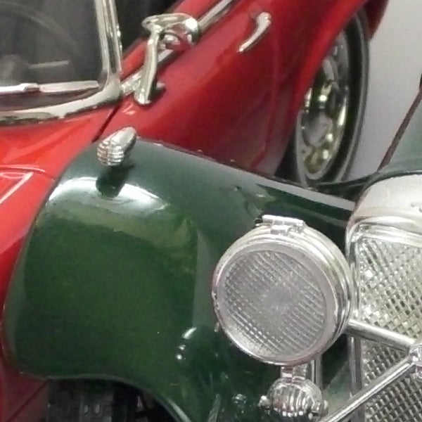 Close-up of vintage red and green cars with chrome headlights.