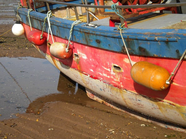 Old boat with colorful hull and buoys on shore.