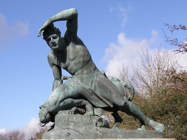 Bronze statue of a figure wrestling a bull outdoors.