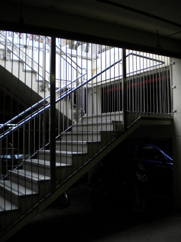 Underexposed image of a parking garage staircase with vehicles.