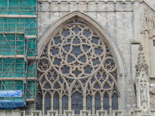 Intricate gothic cathedral window with scaffolding on the left side.