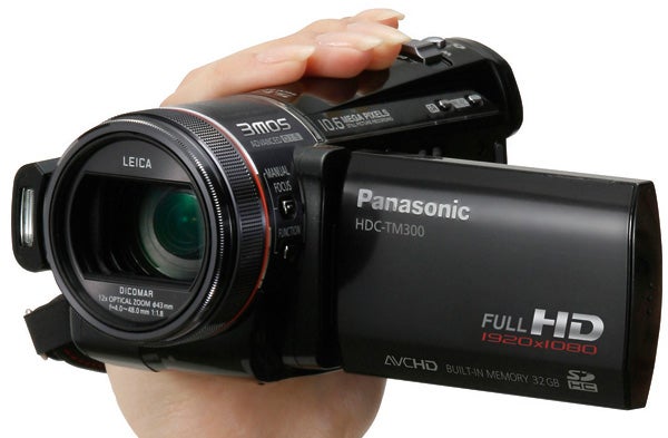 Hand holding Panasonic HDC-TM300 camcorder with lens visible.