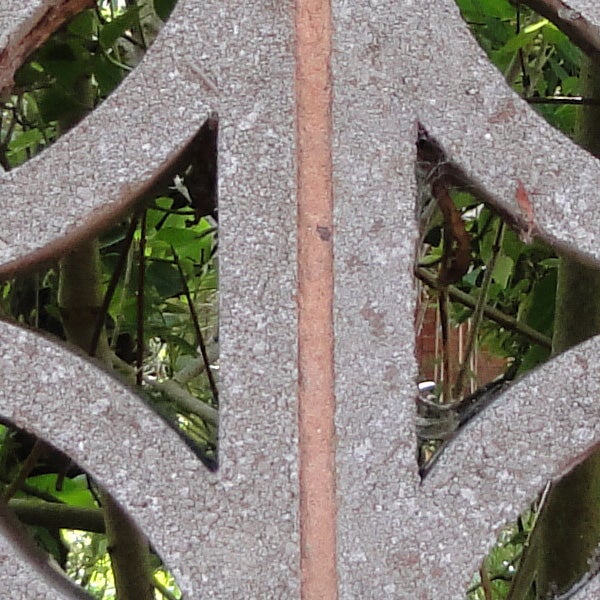 Close-up of weathered metal fence with foliage background.