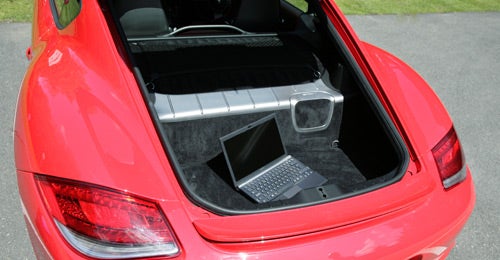 Red Porsche Cayman with open trunk and laptop inside.Porsche Cayman 2.9 PDK rear trunk open showing storage space.