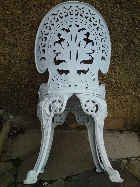 White ornate cast-iron chair against a wall.
