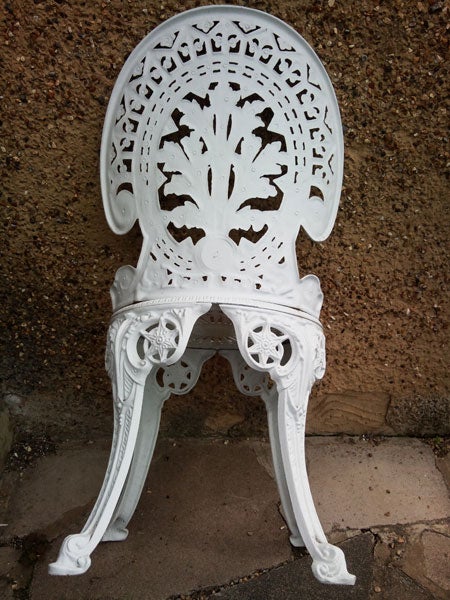 White ornate cast iron chair against a brown wall.