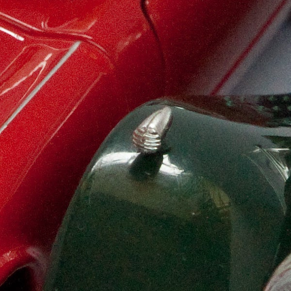 Close-up of a hood ornament with red car in background.