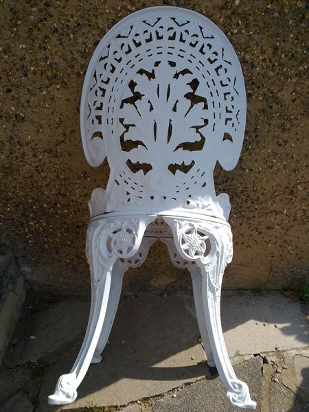 White ornate cast iron chair against a concrete wall.