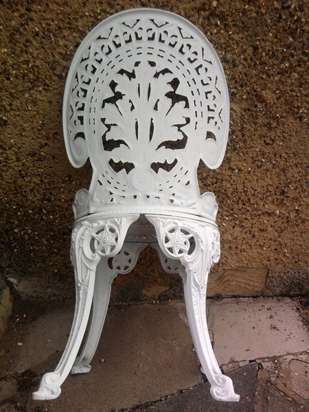 Intricately designed white iron garden chair against a wall.