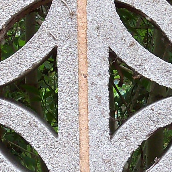 Close-up of leafy background through decorative concrete pattern.