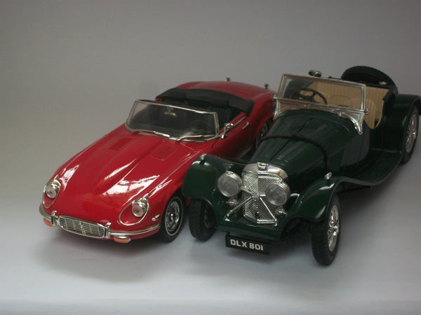 Two model vintage cars on a white surface.