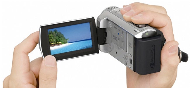 Hands holding Sony Handycam DCR-SX30E with screen displaying beach scenery.