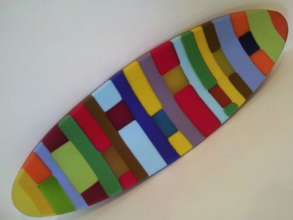 Colorful surfboard-shaped art installation on a white wall.