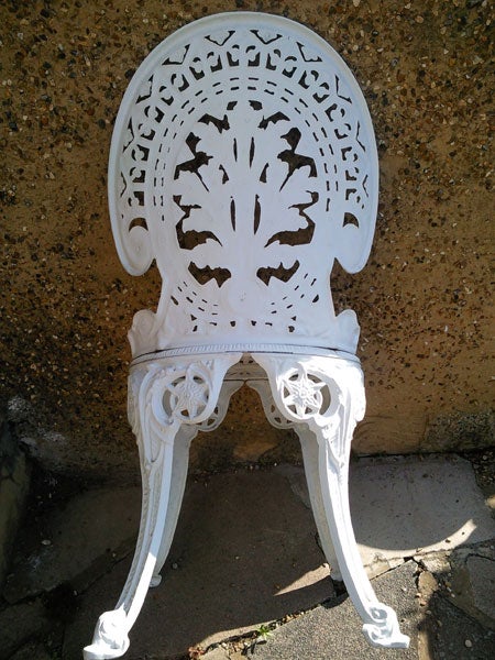 White ornate outdoor chair against a concrete wall.