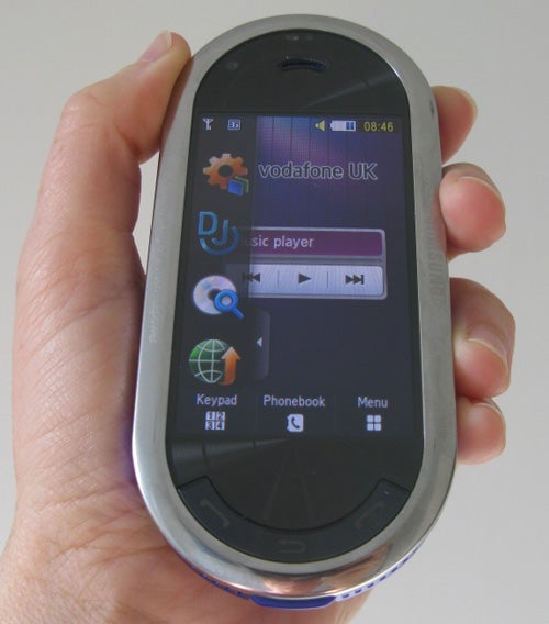 Hand holding a Samsung M7600 Beat DJ phone with screen on.