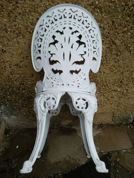 White ornate metal chair on a concrete surface.