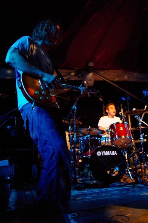Guitarist and drummer performing on stage at night.