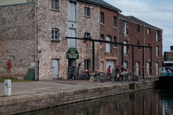 Photo of a waterfront scene with people and bicycles near old buildings.