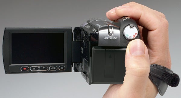 Hand holding Panasonic HDC-HS200 camcorder with LCD screen open.