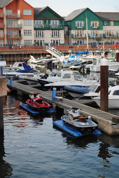 Marina with boats and jet skis, colorful buildings in background.