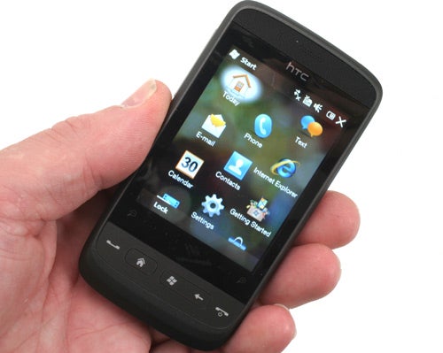 Hand holding an HTC Touch2 smartphone displaying the home screen.