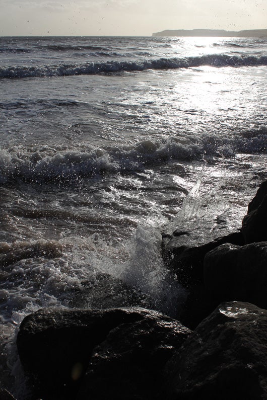 Seascape with sunlight reflection and splashing waves on rocks