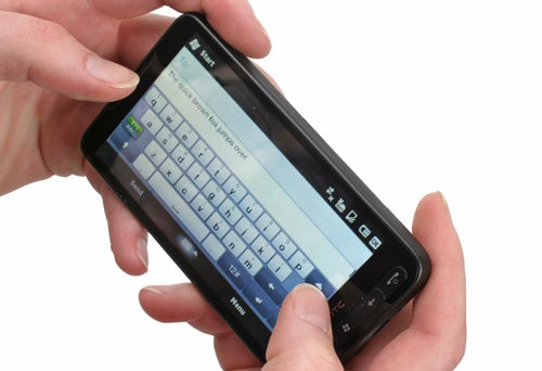Hands holding an HTC HD2 smartphone displaying keyboard.