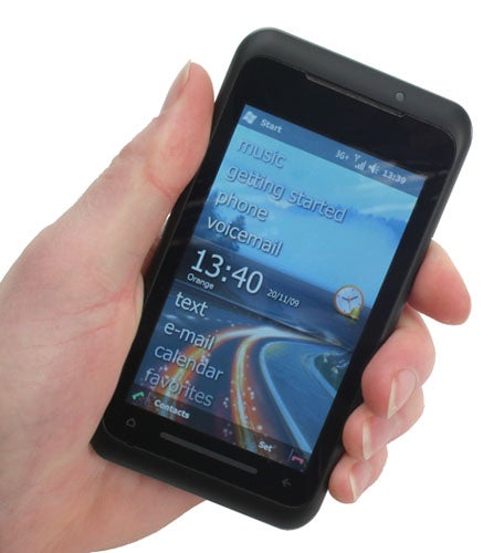 Hand holding Toshiba TG01 smartphone displaying home screen.