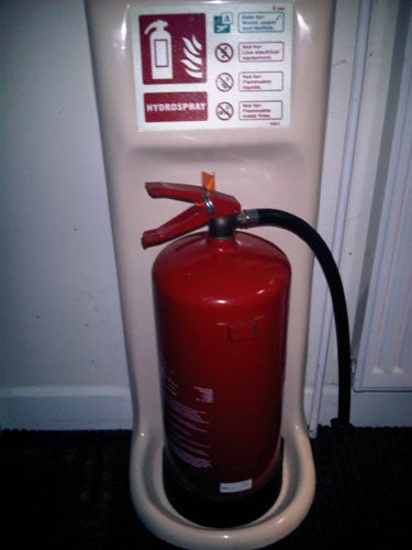 Fire extinguisher placed on floor stand against white wall.