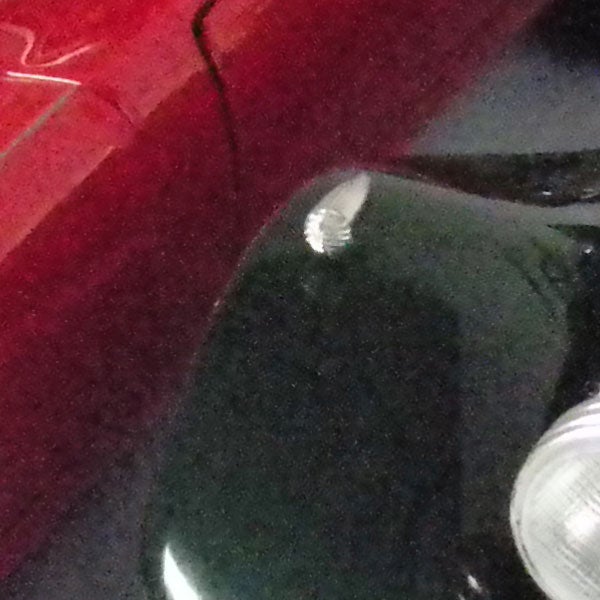 Car with reflective red paint and headlight visible.