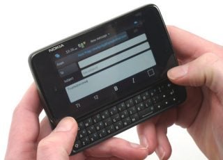 Hands holding a Nokia N900 smartphone with keyboard extended.