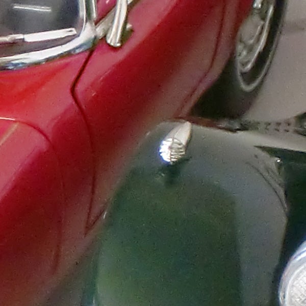 Close-up of a red and a green toy car's front ends.