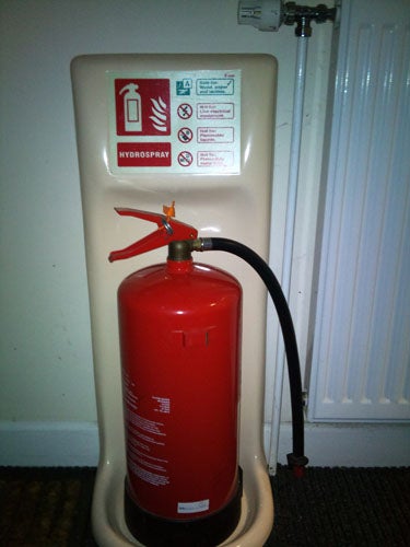 Red fire extinguisher with instructional label on stand.