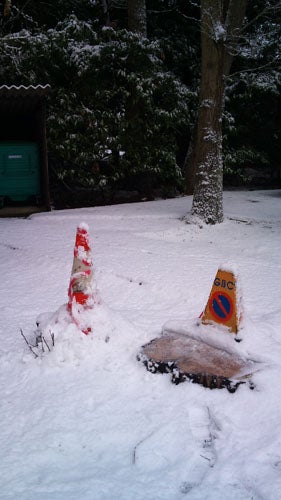 Snow-covered ground with traffic cone and red bollard.