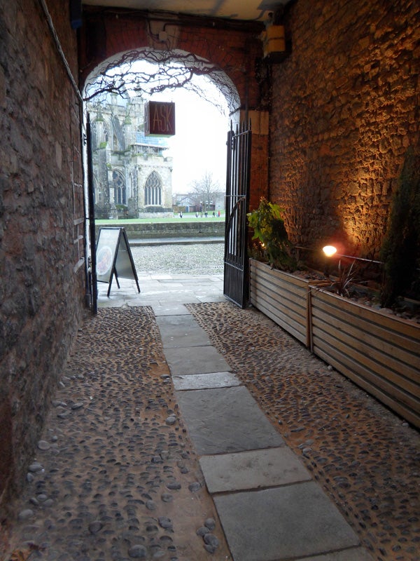 Stone alleyway leading to cathedral and garden.