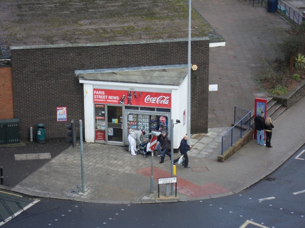 Street view of a newsstand taken from above with people around.