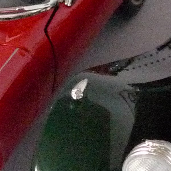 Close-up of a classic car hood ornament and reflections.