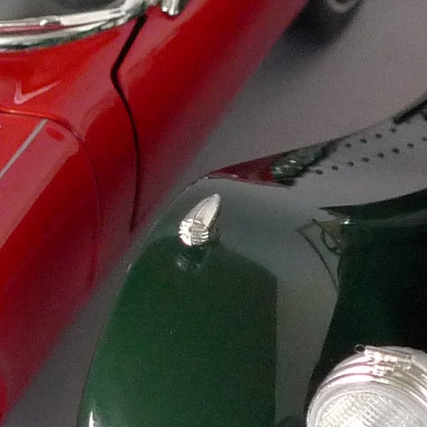 Close-up of red and green vintage cars' hoods and emblems.
