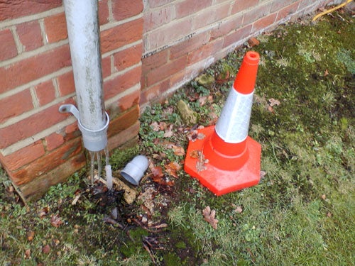 Traffic cone next to a downspout on wet grass.