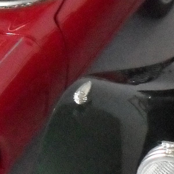 Close-up of a screw on a red car surface.