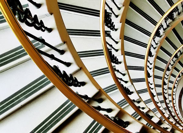 Spiral staircase looking downwards with graphic shadows.