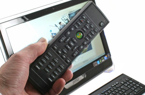 Hand holding remote control in front of MSI Wind Top computer.