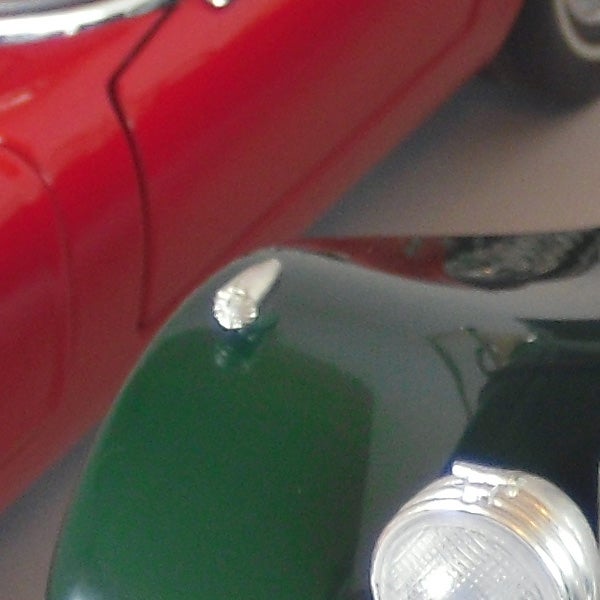 Close-up of red and green cars with reflection.